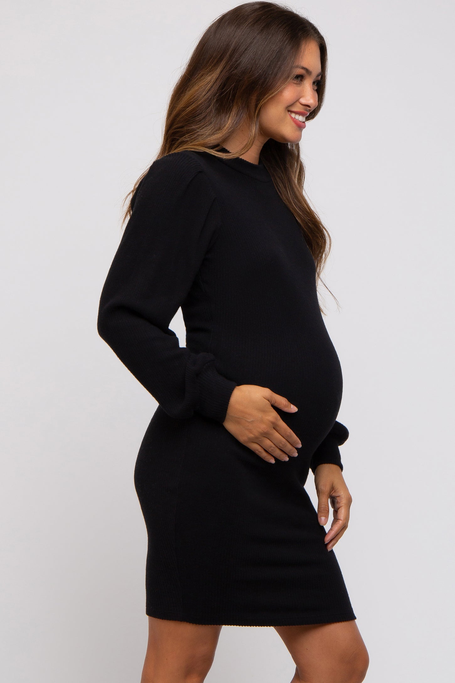 woman wearing a black ribbed maternity dress, smiling and holding her baby bump