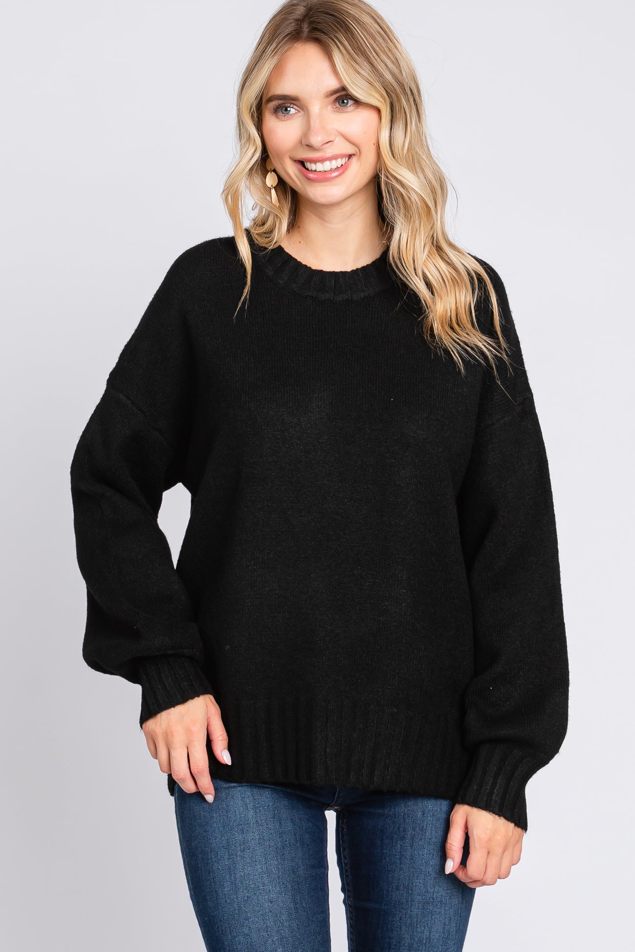 woman wearing a black oversized sweater with long sleeves and a ribbed hem, smiling at the camera