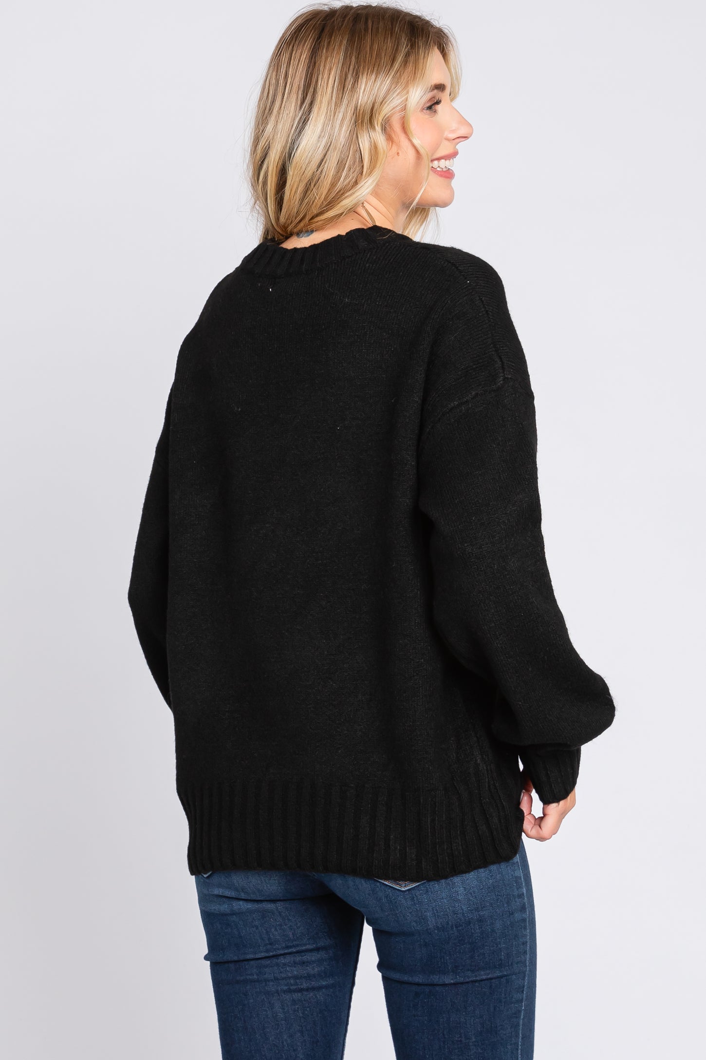 woman wearing a black oversized sweater with ribbed hem and a relaxed fit, seen from the back