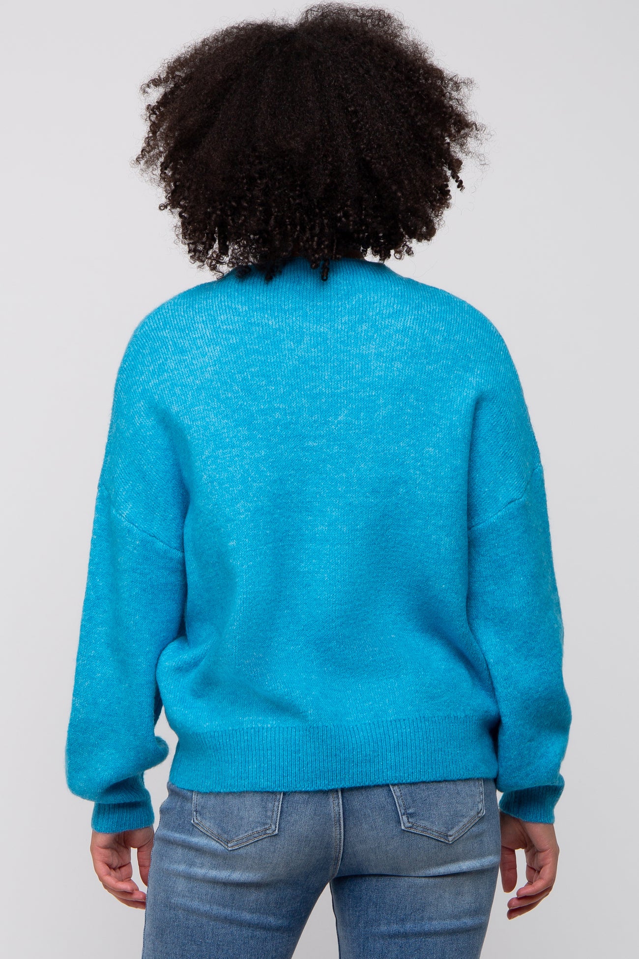 woman wearing a bright blue oversized sweater with a relaxed fit and long sleeves, viewed from the back