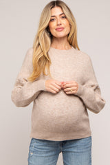 woman wearing a beige maternity sweater and holding her baby bump, paired with light blue jeans