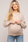 woman wearing a beige maternity sweater and holding her baby bump, paired with light blue jeans