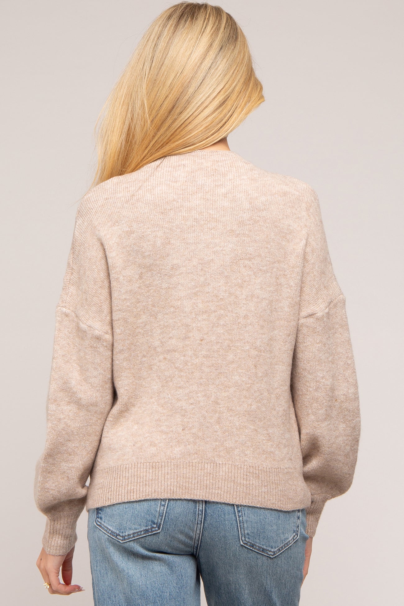 woman wearing a cozy beige maternity sweater with a relaxed fit and balloon sleeves, seen from the back