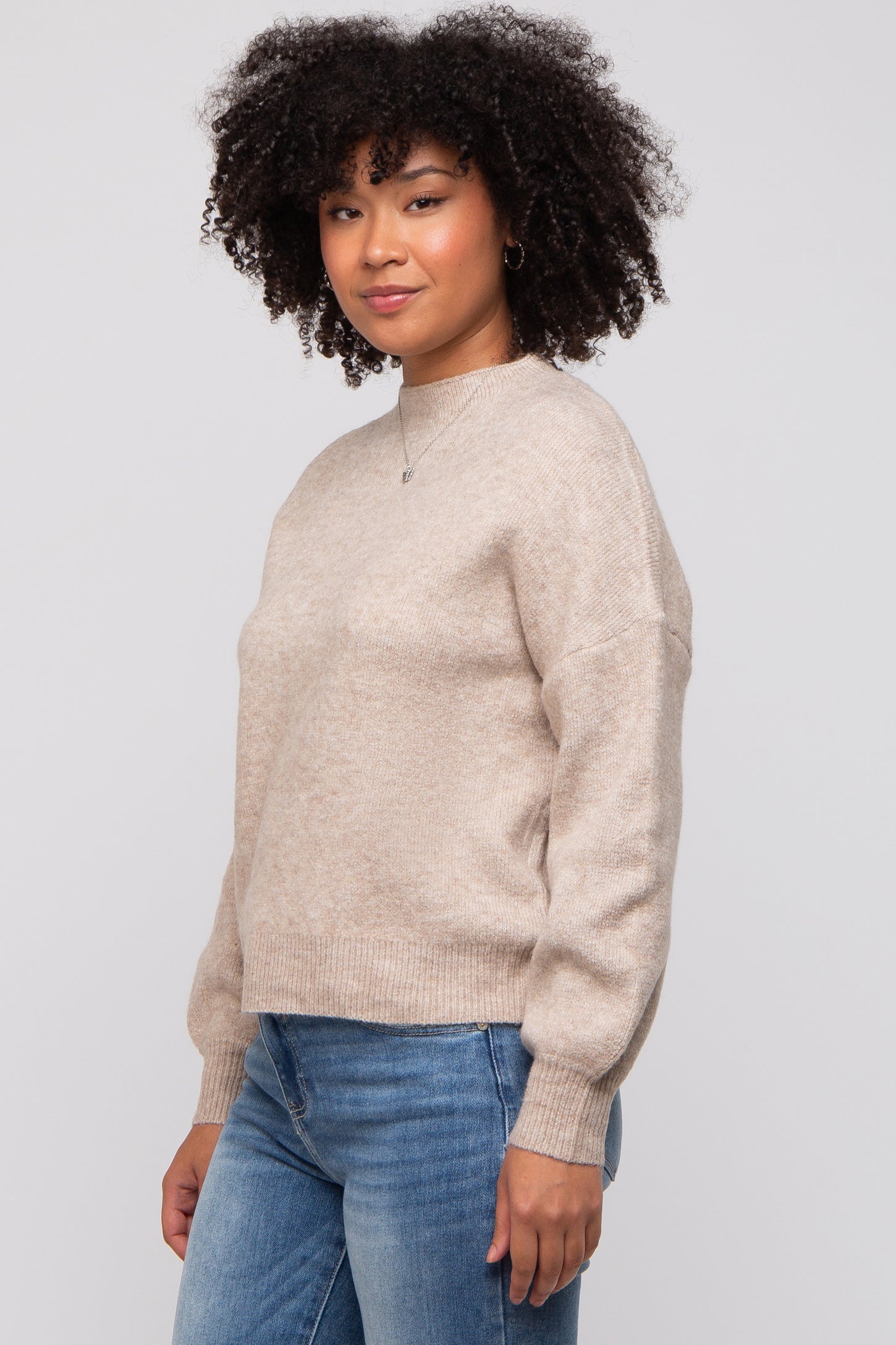 woman wearing a beige knitted sweater with a relaxed fit and long sleeves paired with blue jeans