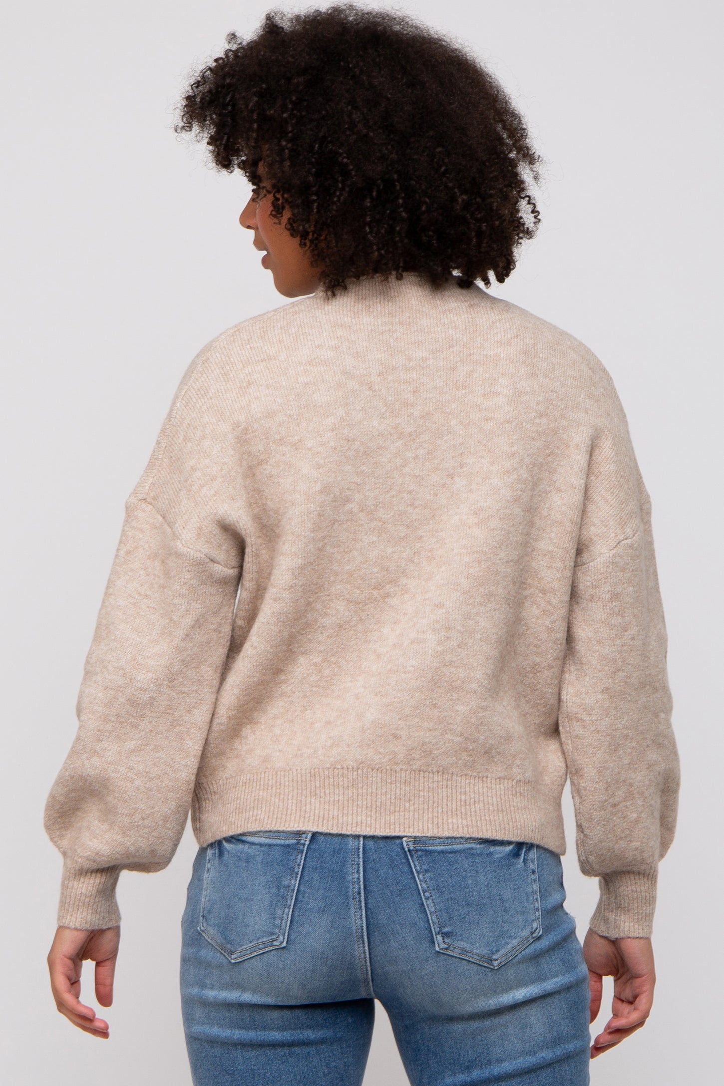 woman wearing a beige oversized sweater with balloon sleeves, seen from the back, paired with light blue jeans