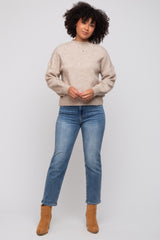 woman wearing a beige sweater and blue jeans, standing with hands clasped in front, paired with tan ankle boots