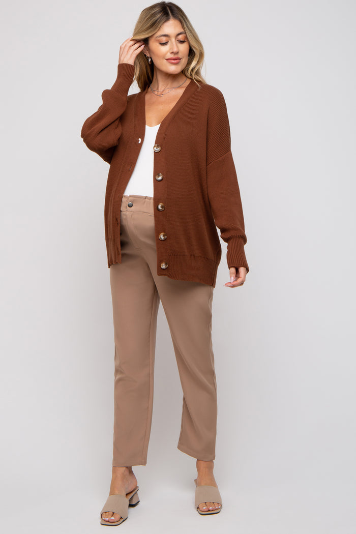 woman wearing a rust brown maternity cardigan over a white top with button details and beige maternity pants