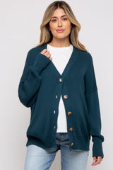 woman wearing a dark teal cardigan with buttons over a white t-shirt and light blue jeans, no visible baby bump