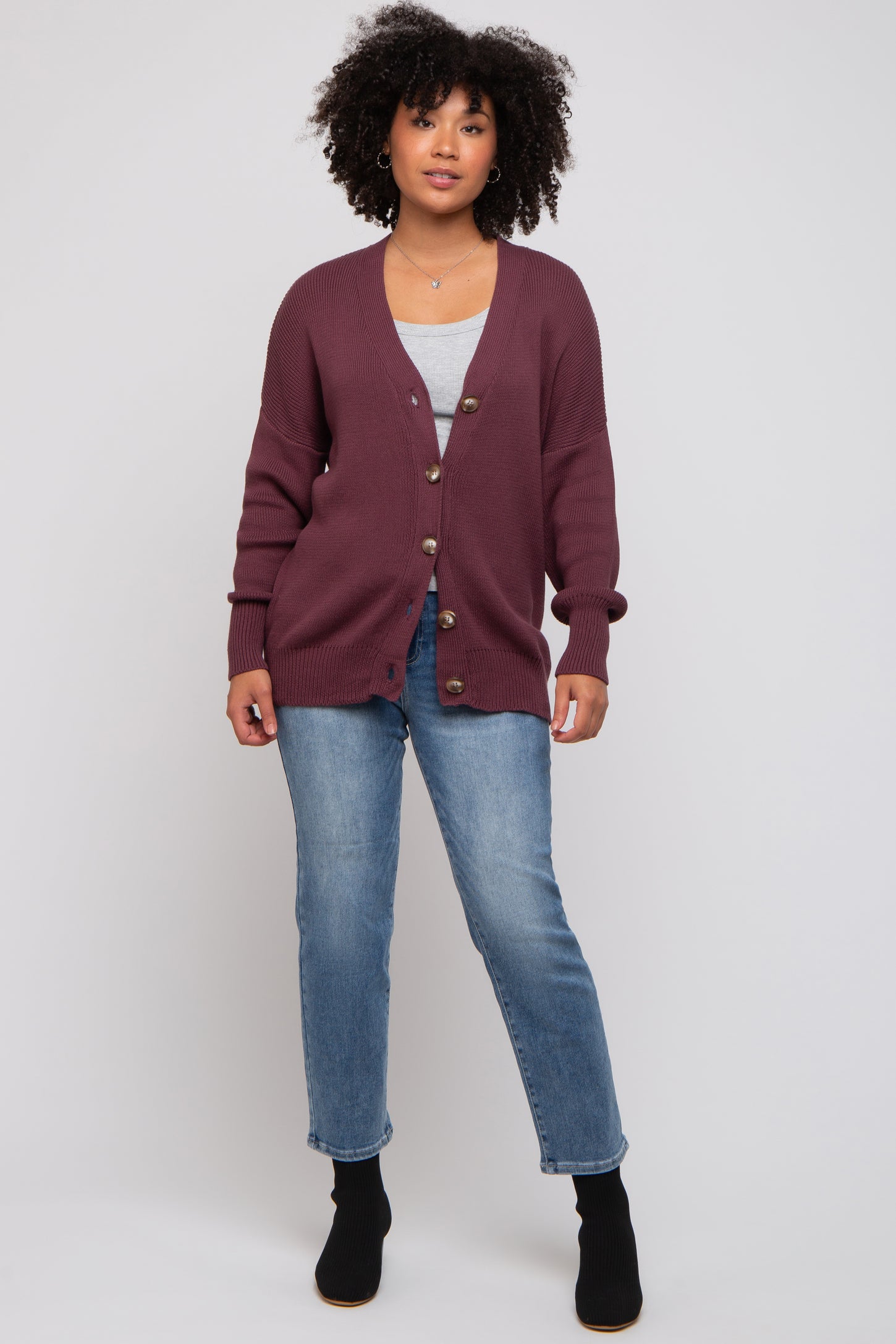 woman wearing a burgundy knit cardigan with buttons, paired with a gray top and blue jeans