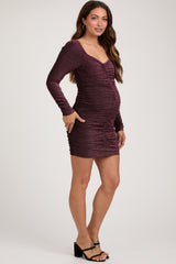 woman wearing a burgundy shimmer long sleeve maternity dress with ruching and a visible baby bump