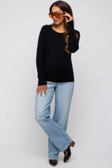 woman wearing a black long sleeve maternity top and light blue flared jeans with sunglasses, showcasing her baby bump