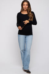 woman wearing a black long sleeve maternity top and light blue flared jeans, holding sunglasses