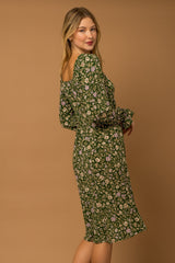 woman wearing a green floral midi dress with puff sleeves and a fitted waist, posing against a beige background