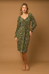 woman wearing a green floral print dress with a ruched front and long sleeves, standing against a neutral background