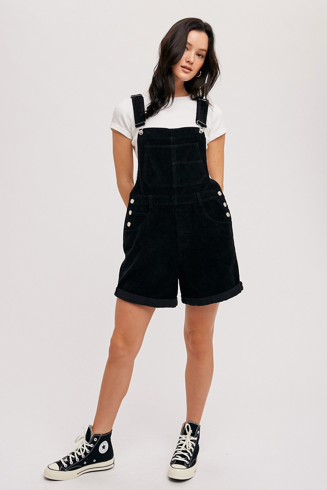 woman wearing black corduroy overalls with rolled hems, paired with a white t-shirt and black high-top sneakers