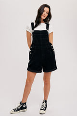 woman wearing black corduroy overalls with rolled hems, paired with a white t-shirt and black high-top sneakers