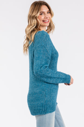 woman wearing a cozy teal oversized sweater with a loose fit and long sleeves, smiling while facing sideways