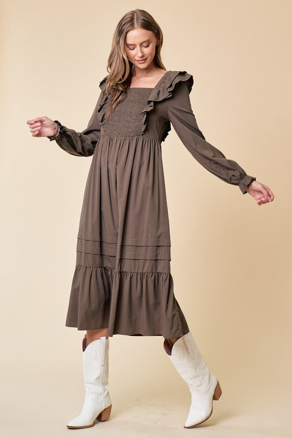 woman wearing a brown long sleeve dress with ruffle details and a smocked bodice, paired with white cowboy boots