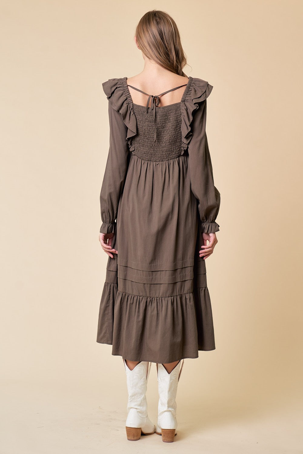 woman wearing a brown long sleeve dress with ruffle details and tiered hem, paired with white cowboy boots