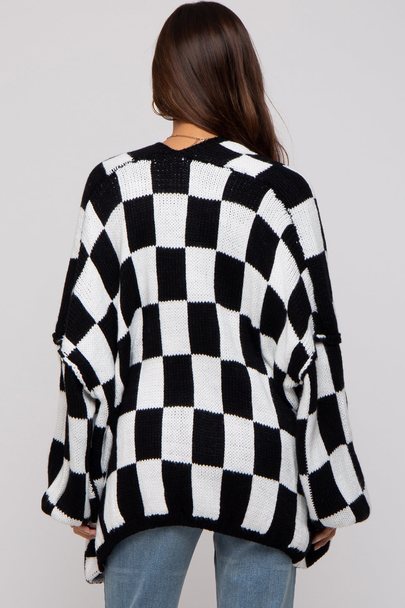 woman wearing a black and white checkered maternity sweater, with loose fit and open sleeves, viewed from the back