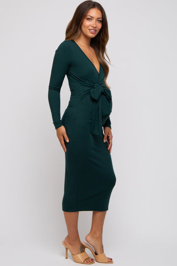 woman wearing a dark green long sleeve maternity dress with a tied waist and a visible baby bump