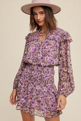 woman wearing a purple floral smocked mini dress with ruffle details and long sleeves, paired with a wide-brimmed hat