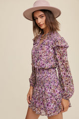 woman wearing a purple floral ruffled mini dress with a smocked waist and long sleeves, accessorized with a wide-brimmed hat