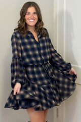woman wearing a navy blue and tan plaid shirt dress with long sleeves and a belted waist, twirling playfully