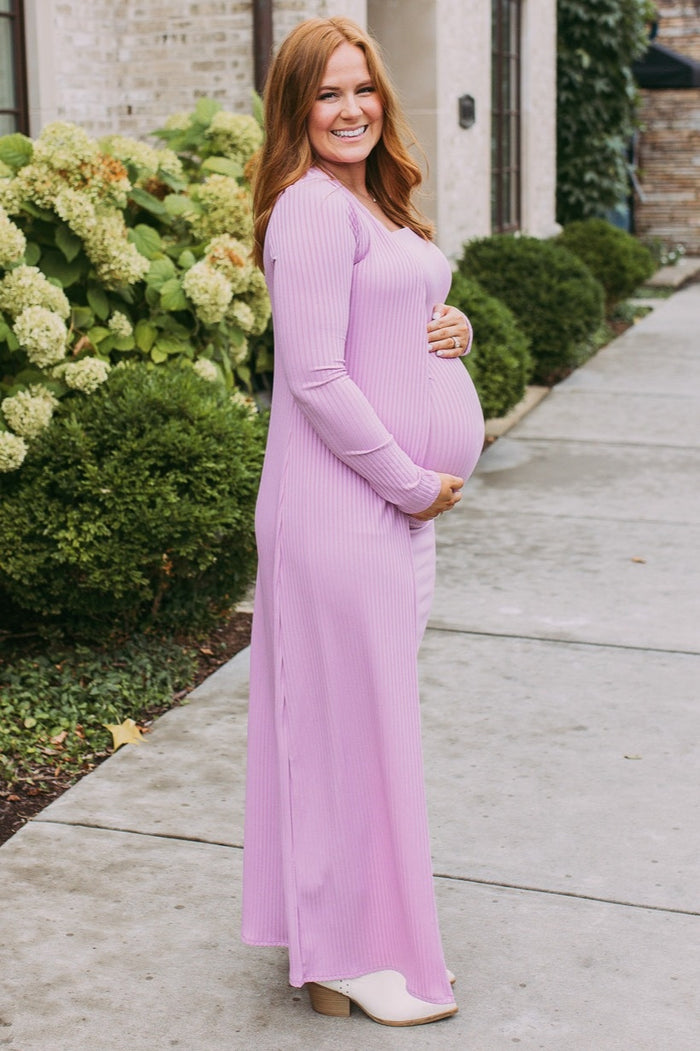 woman wearing a light pink ribbed maternity maxi dress and showcasing her baby bump while smiling outdoors