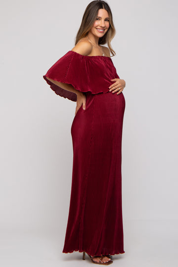 woman wearing a burgundy off-shoulder maternity maxi dress, gently holding her baby bump