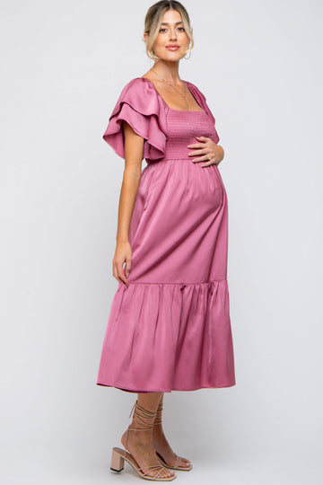 woman wearing a dusty rose maternity dress with flutter sleeves and a tiered skirt, holding her baby bump
