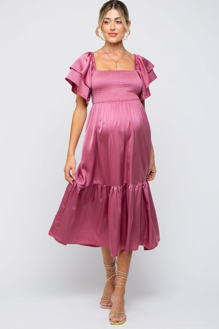 woman wearing a rose pink maternity dress with ruffled sleeves and a smocked bodice, highlighting her baby bump