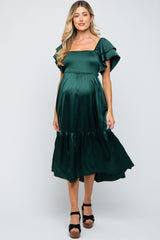 woman wearing a dark green maternity dress with flutter sleeves and a smocked bodice, showcasing her baby bump