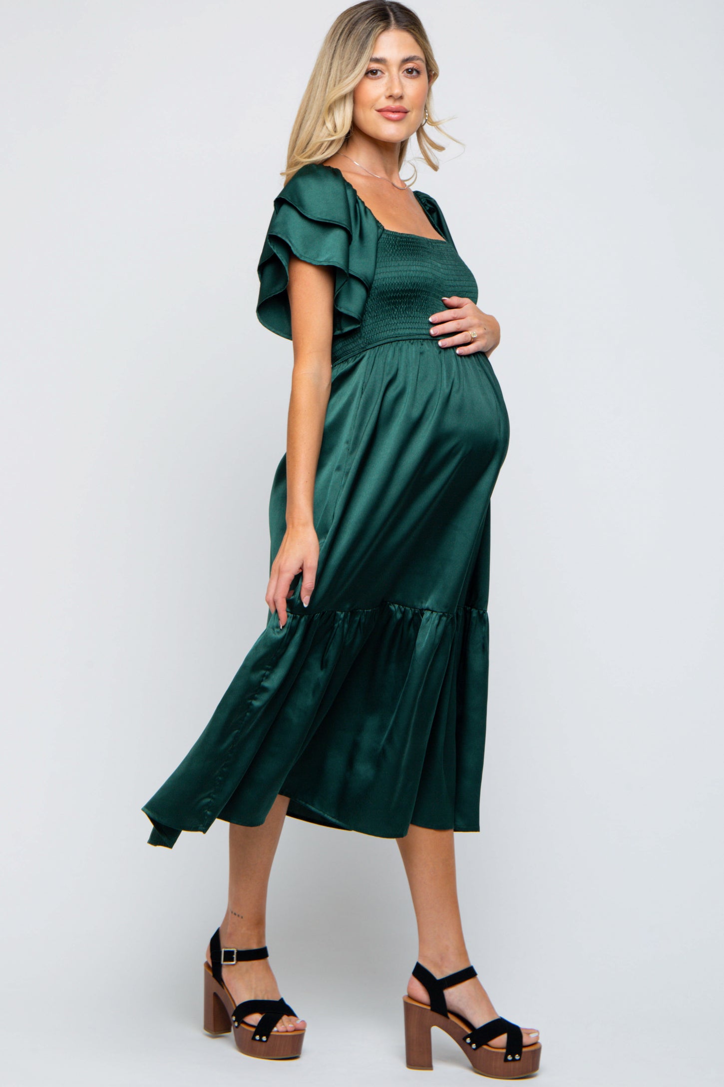 woman wearing a dark green maternity dress with flutter sleeves and a gathered waist, showing a baby bump