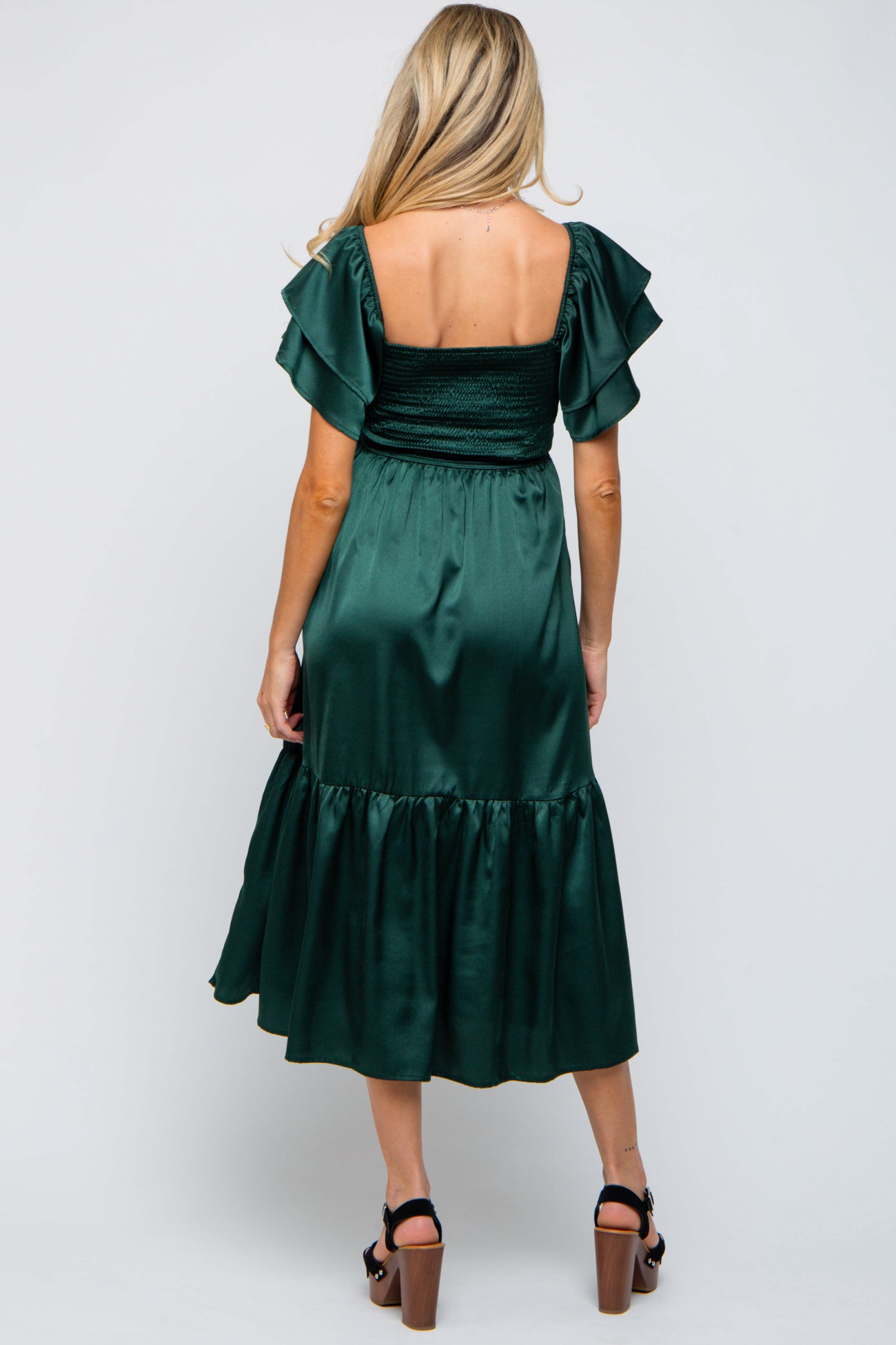 woman wearing a dark green maternity dress with ruffled sleeves and a tiered skirt, showcasing her baby bump from the back