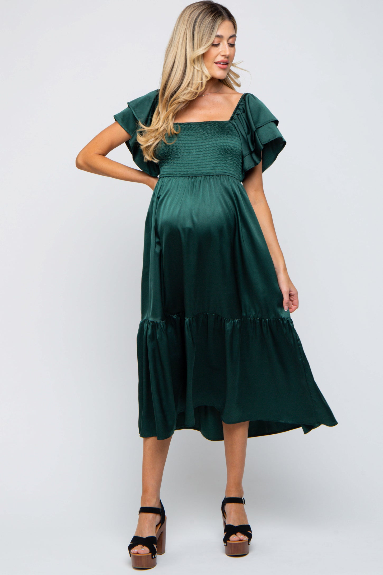 woman wearing a dark green maternity dress with flutter sleeves and a tiered skirt, showcasing her baby bump