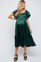 woman wearing a dark green maternity dress with flutter sleeves and a tiered skirt, showcasing her baby bump