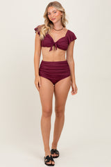 woman wearing a burgundy two-piece swimsuit with ruffled sleeves and high-waisted bottom, standing on a neutral background