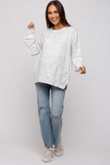 woman wearing a white speckled oversized maternity sweater with relaxed fit and paired with distressed light wash jeans