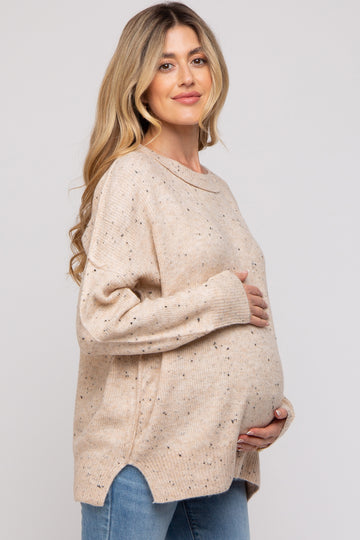 woman wearing a beige maternity sweater with speckled details and holding her baby bump