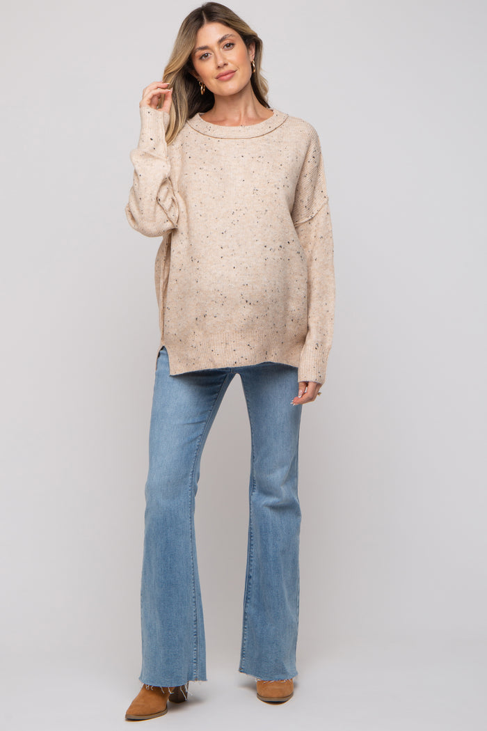 woman wearing a beige maternity sweater with speckled details and blue flared jeans, showing her baby bump