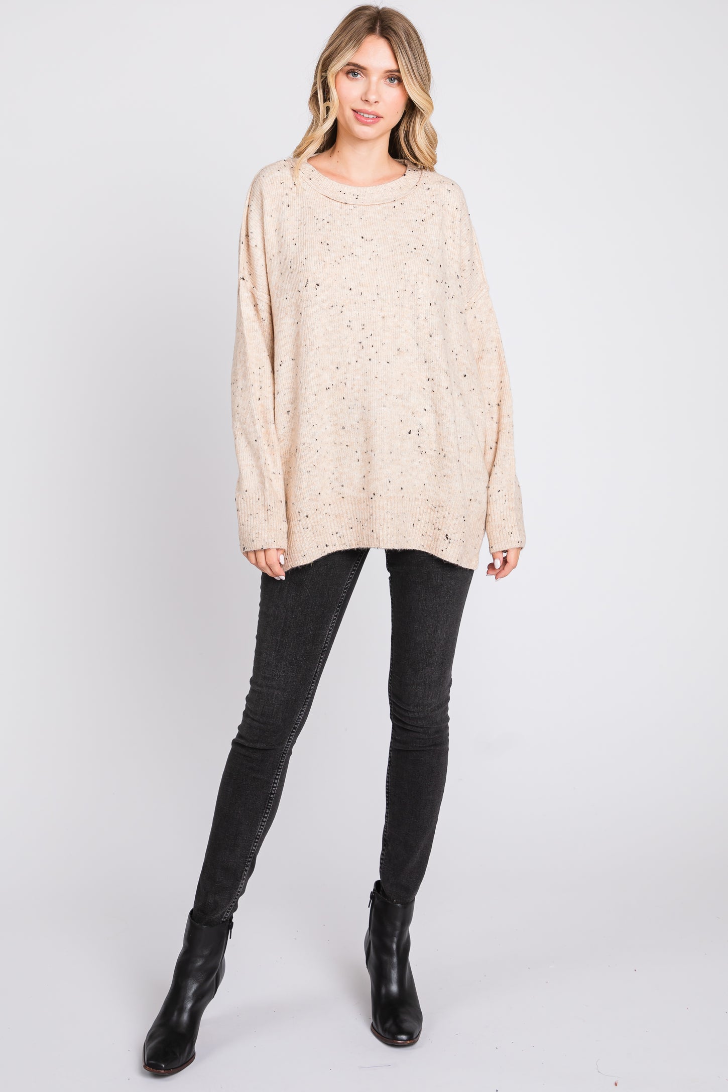 woman wearing a beige oversized sweater with speckled details and black skinny jeans