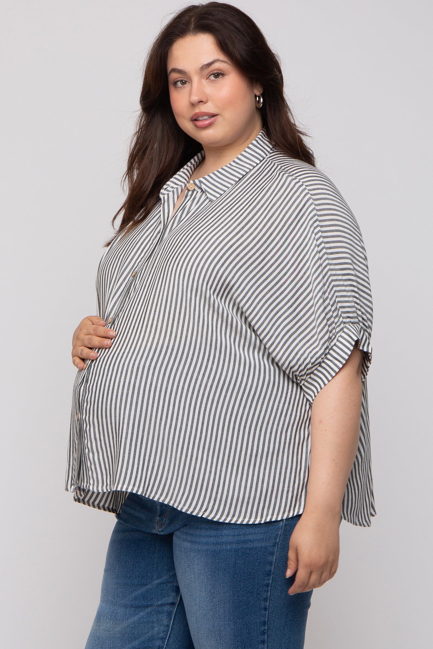 woman wearing a striped maternity plus blouse with a loose fit and short sleeves, highlighting her baby bump
