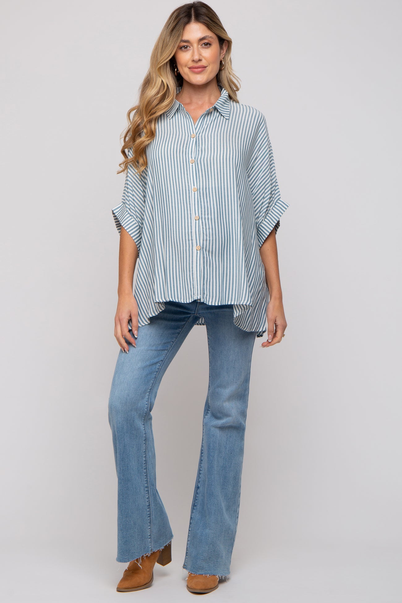 woman wearing a light blue striped button-up maternity shirt and flared jeans, displaying her baby bump