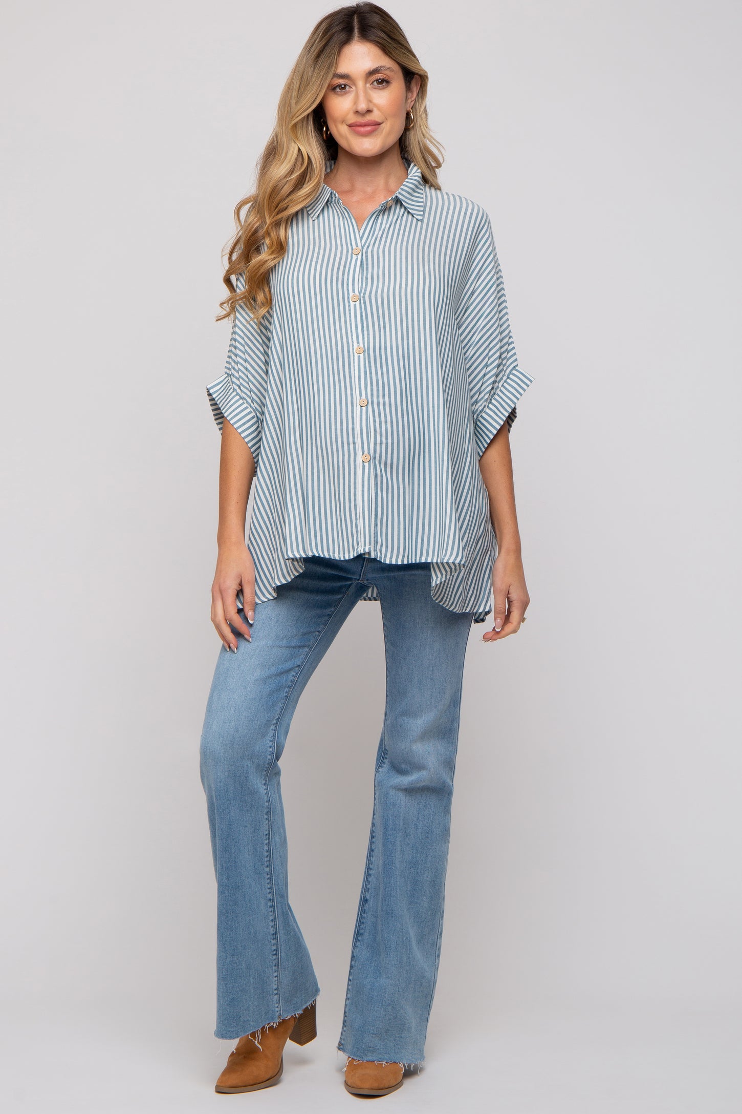 woman wearing a light blue striped button-up maternity shirt and flared jeans, displaying her baby bump
