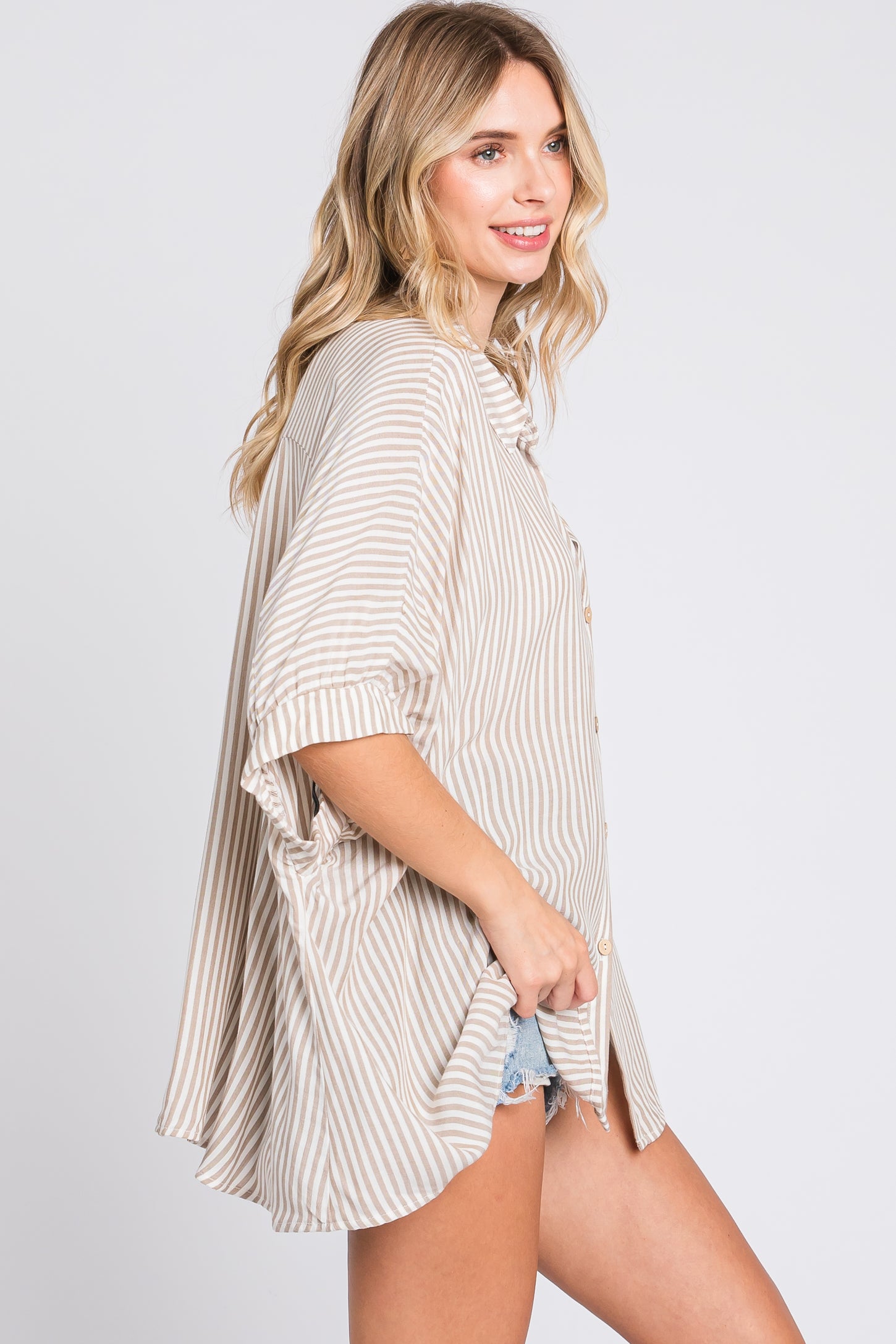 woman wearing a beige and white striped oversized button-up shirt with short sleeves and a curved hemline
