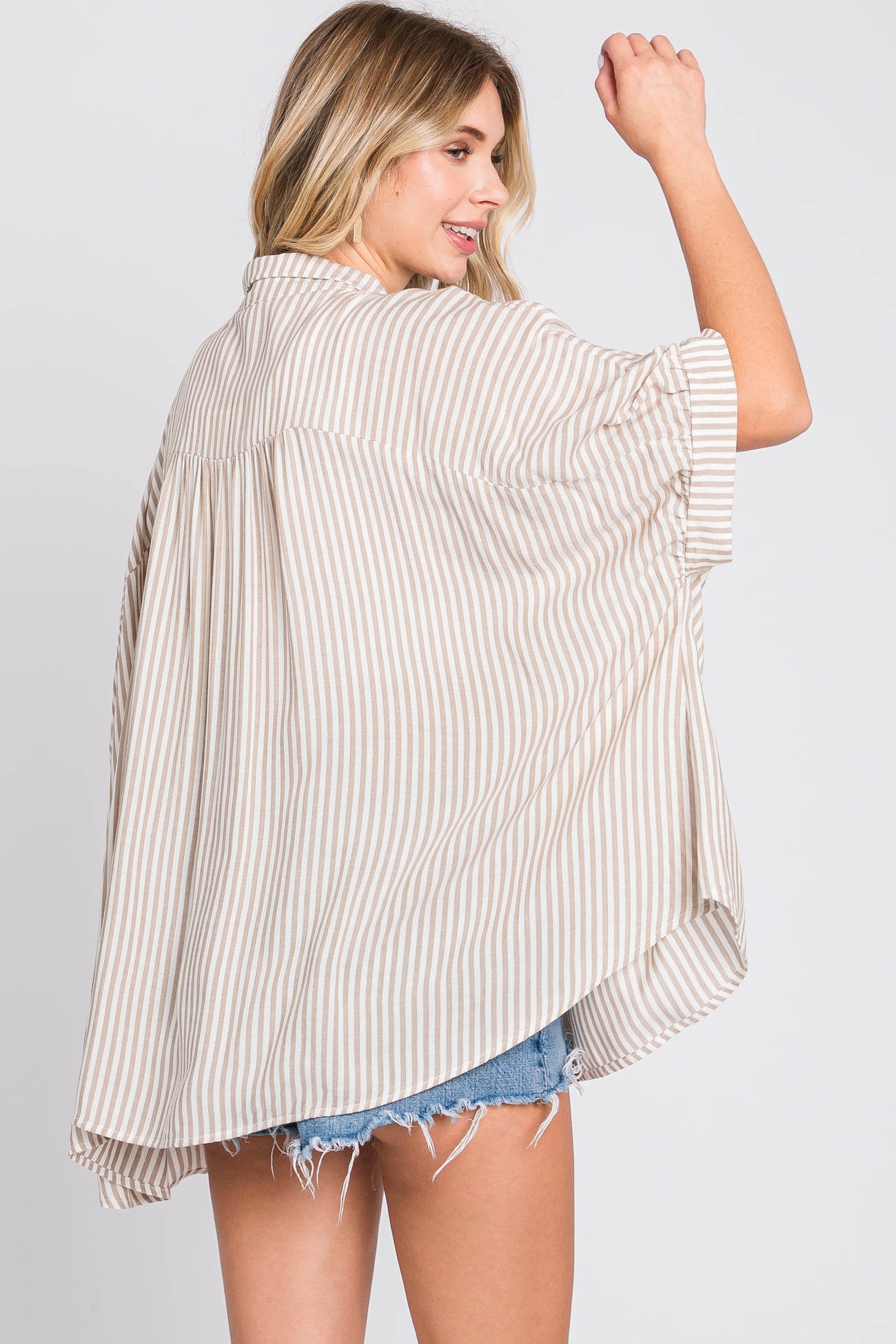 woman wearing a light beige and white striped oversized shirt with short sleeves and a flowy back, styled with denim shorts