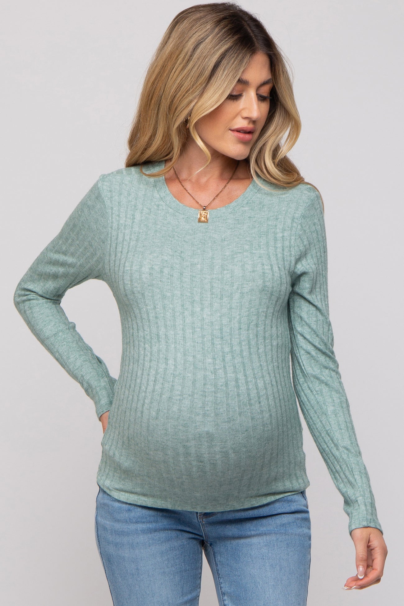 woman wearing a light green ribbed maternity top and showing her baby bump while posing