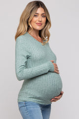 woman wearing a light green ribbed maternity sweater and cradling her baby bump
