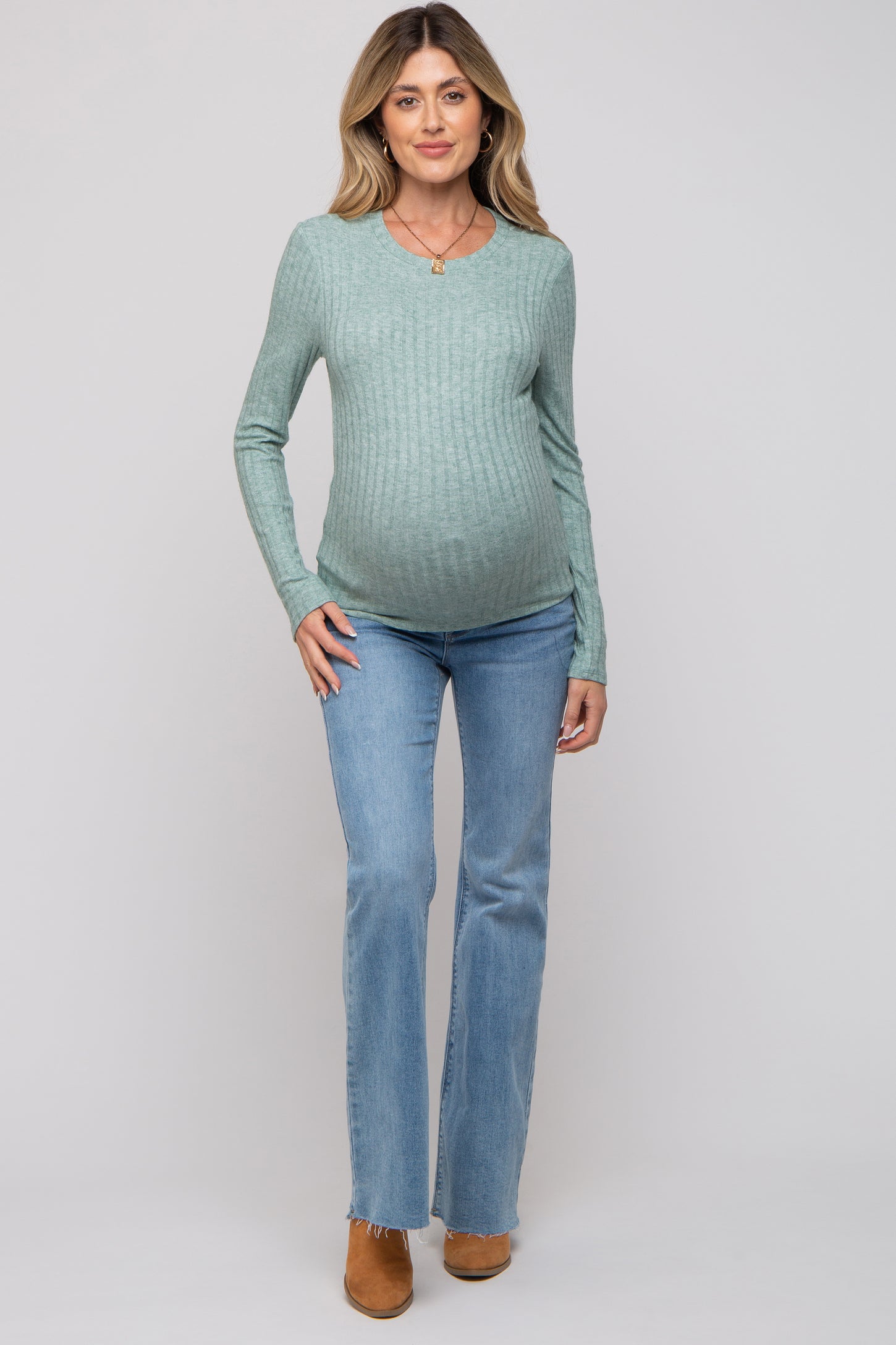 woman wearing a light green long sleeve maternity top and blue flared maternity jeans with visible baby bump